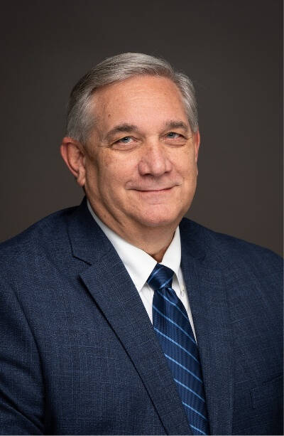 A man looks into a camera. He is wearing a blue suit and tie.